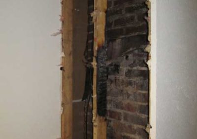 Damaged wood framing in room with brick wall behind it