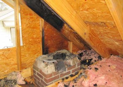 pink insulation on floor around a broken masonry chimney with burn stains on ceiling wood