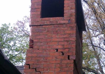 Chimney with cracked broken masonry bricks and trees in the background