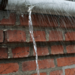 rain coming off of the roof of a home with masonry in the background