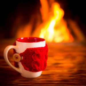 a white coffee cup with a knitted red hand koozie around it in front of a fireplace