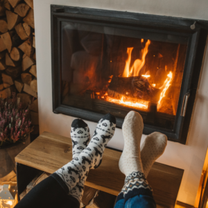 two sets of feet with socks on propped up by a lit fireplace