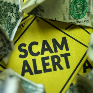 a diamond yellow sign saying "scam alert" surrounded by dollar bills